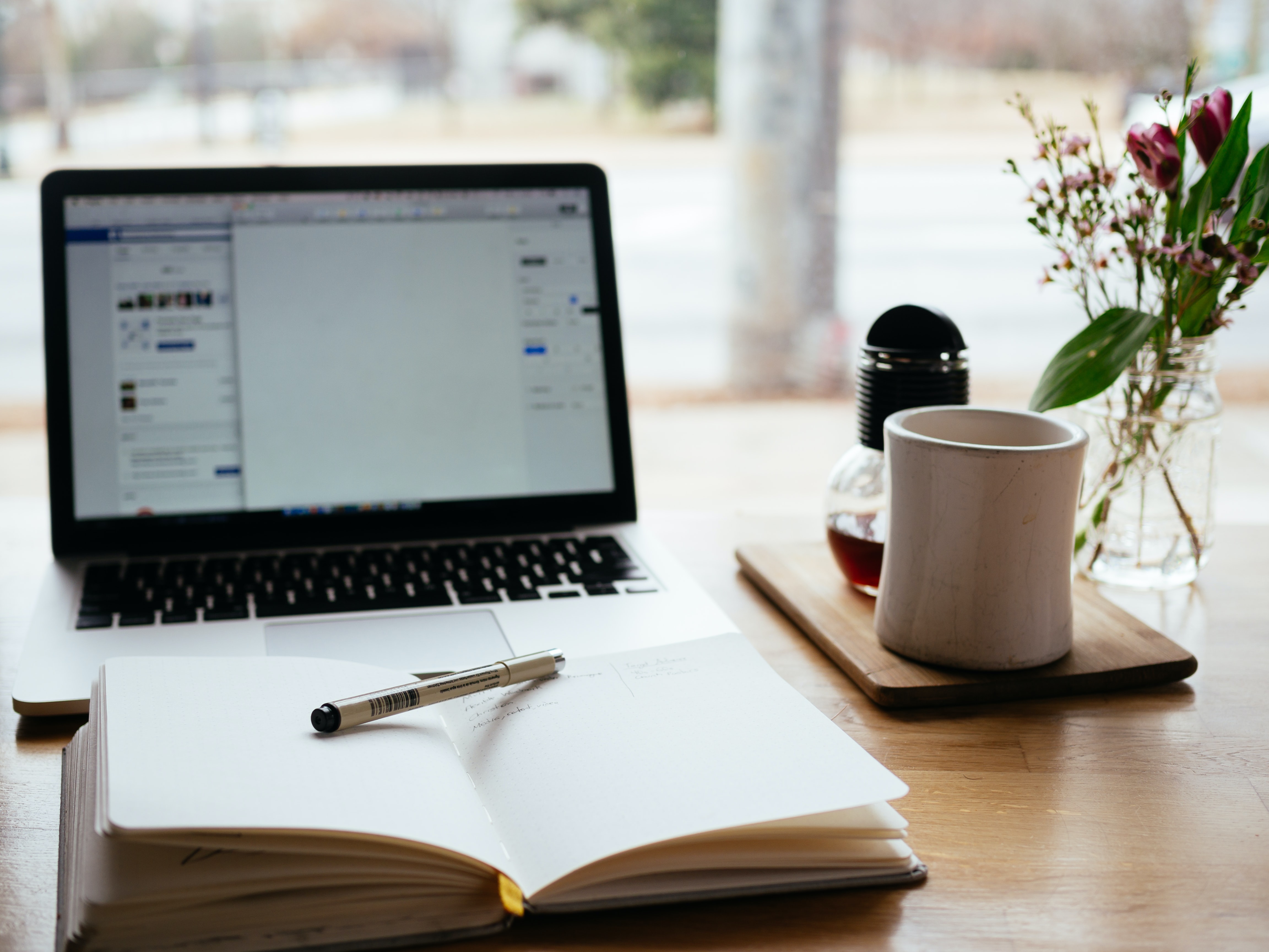 laptop on workdesk with notepad pen coffee cup and flowers
