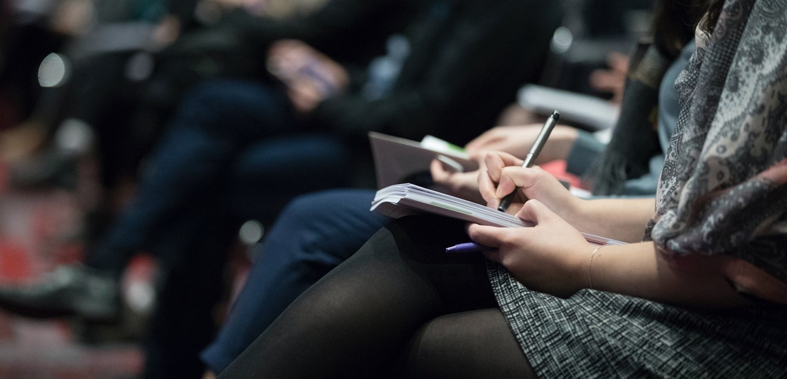 close up of people sat in a seminar taking notes