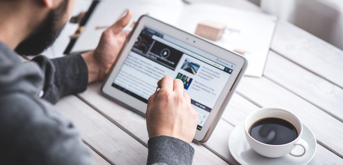 man researching online on ipad with cup of coffee