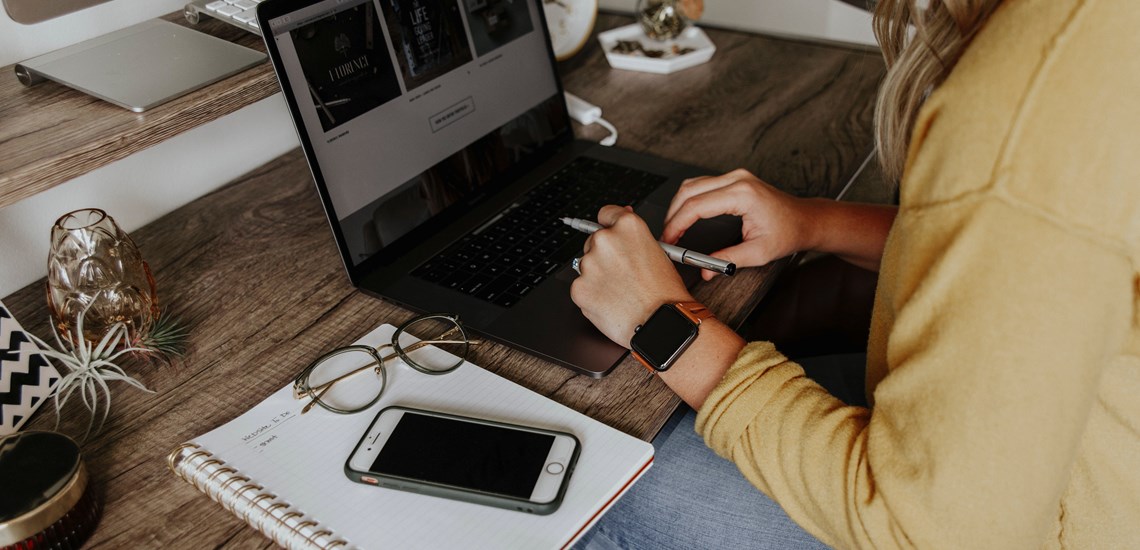 person working at desk with iphone typing on laptop
