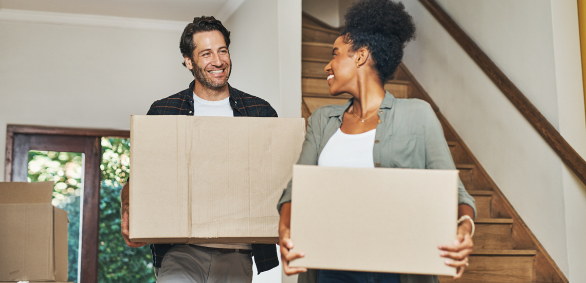 Man and woman holding moving boxes, smiling.