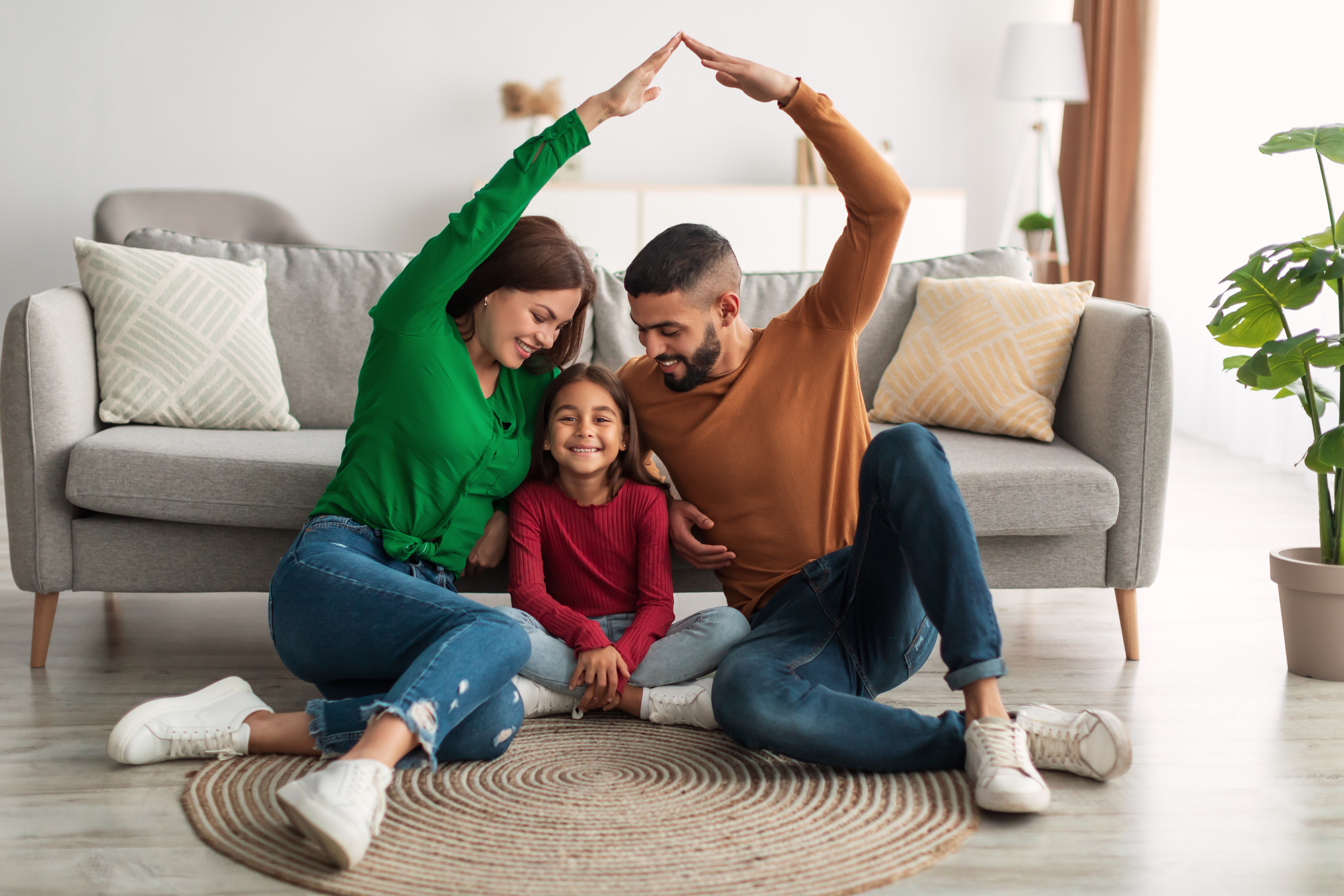 woman and man sitting on floor with hand joined over child to depict protection
